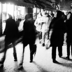 Black and white photo of several groups of people walking past shops