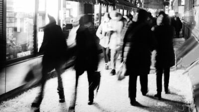 Black and white photo of several groups of people walking past shops