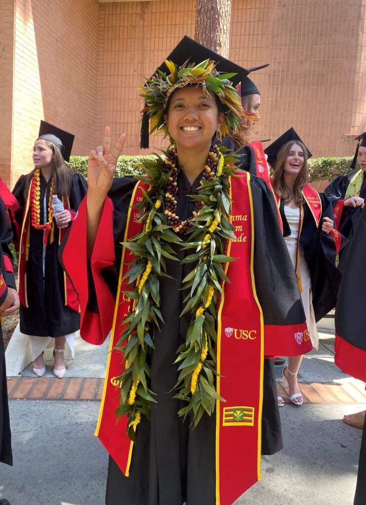 Undergraduate student in regalia, posing with a Fight On sign