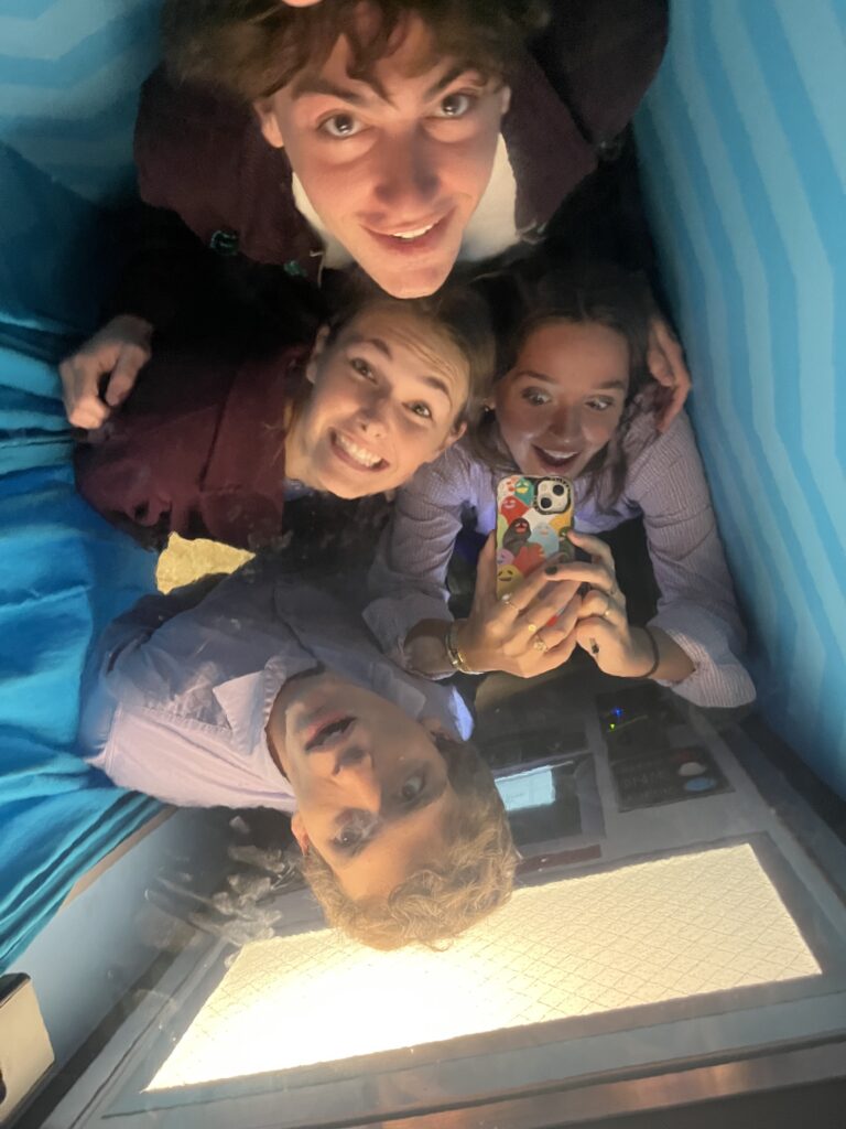 Four students look skyward toward the camera, crammed into a small space