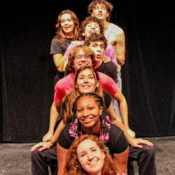 Eight comedians standing in a vertical row