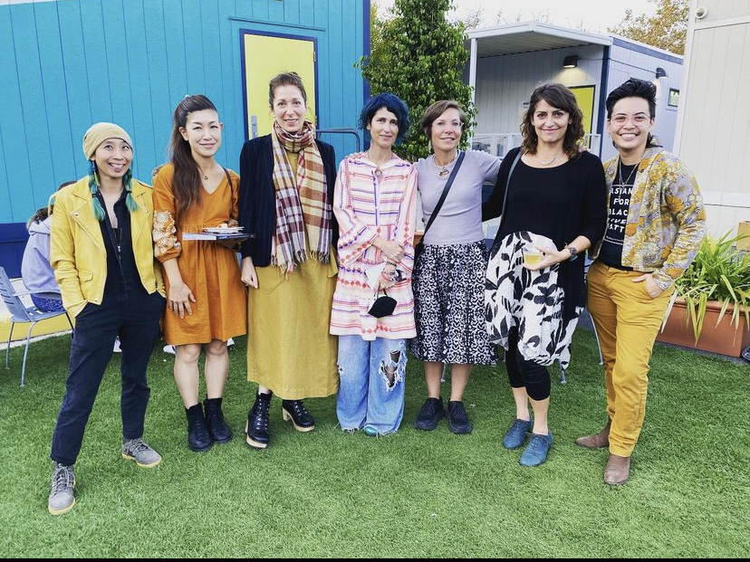 Seven set designers pose side-by-side in front of a blue wall.