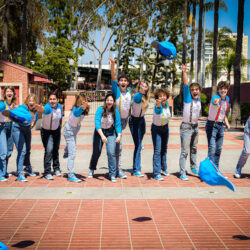 A group of students in blue uniforms toss their baseball caps on USC campus.