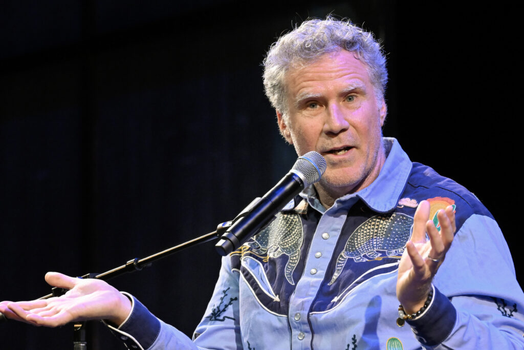 Will Ferrell gestures with his hands upright speaking into a microphone.