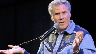 Will Ferrell gestures with his hands upright speaking into a microphone.