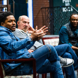 l to r: Sheldon Candis, Rob Schiller, and Bayo Akinfemi sitting in a semicircle and gesturing with their hands.