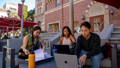 Three students looking over a computer screen in University Village.