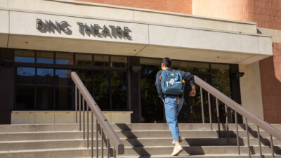 A student rushes up the stairs toward the Bing Theatre.