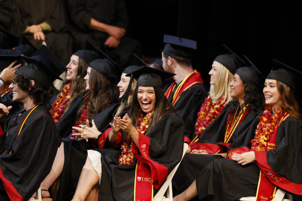 Graduating students laugh and clap at the Commencement ceremony in full regalia.