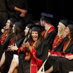 SDA students in commencement regalia laugh and clap at the 2024 Commencement ceremony.