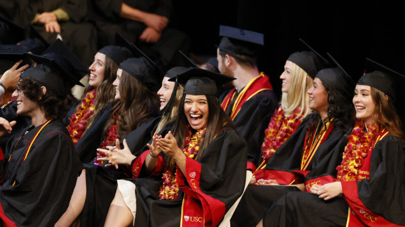 SDA students in commencement regalia laugh and clap at the 2024 Commencement ceremony.