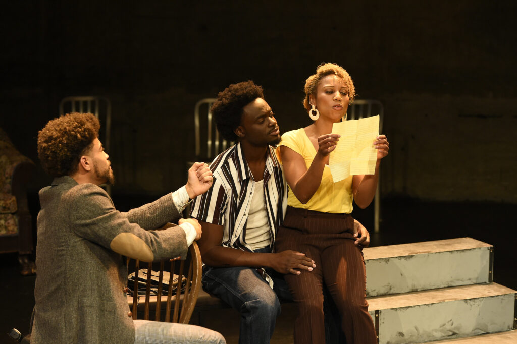 The cast of King Hedley the second perform on stage, with Mister gesturing toward King Hedley and Tonya. Tonya is reading a note while King watches on.