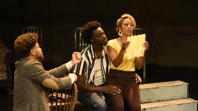 The cast of King Hedley the second perform on stage, with Mister gesturing toward King Hedley and Tonya. Tonya is reading a note while King watches on.