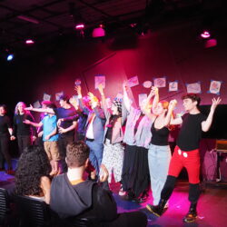 Members of Ludus Remedium onstage with arms clasped in a curtain call.