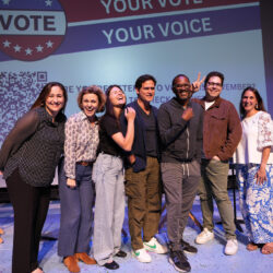 Seven panelists pose for a photo on stage at the 