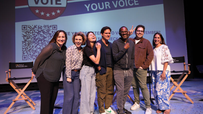 Seven panelists pose for a photo on stage at the 