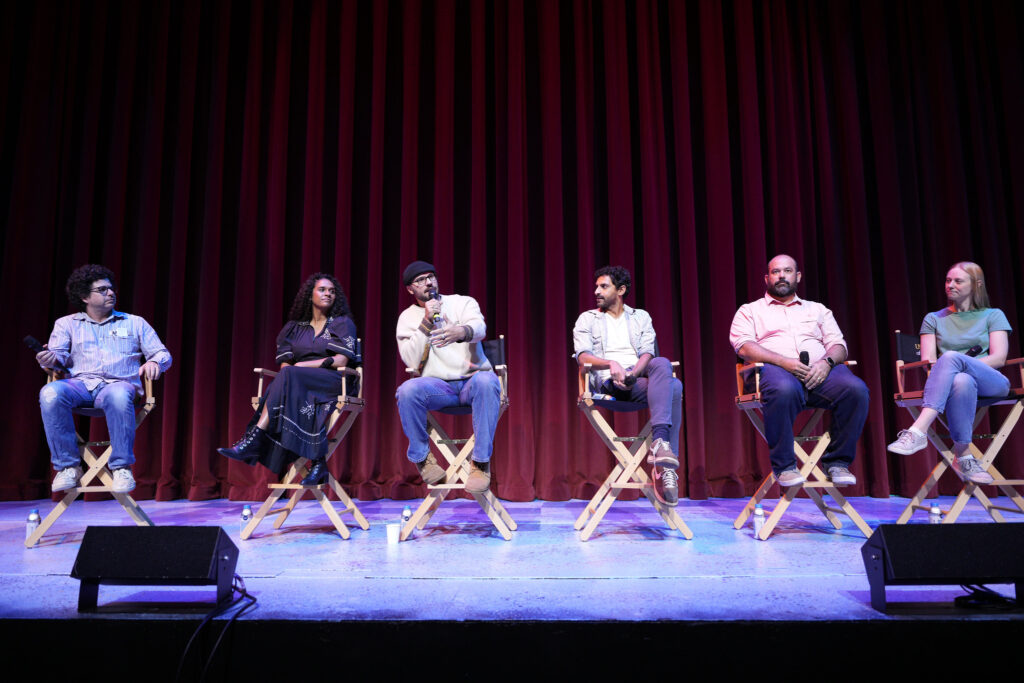 Five panelists and a moderator sitting on chairs on a stage.