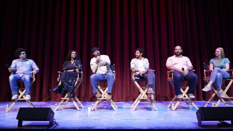 Five panelists and a moderator sitting on chairs on a stage.