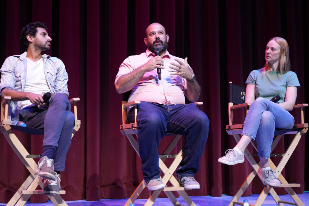 Karan Soni, Tony Shayne and Deborah Ann Woll sit on stage, with Tony Shayne talking into a microphone.