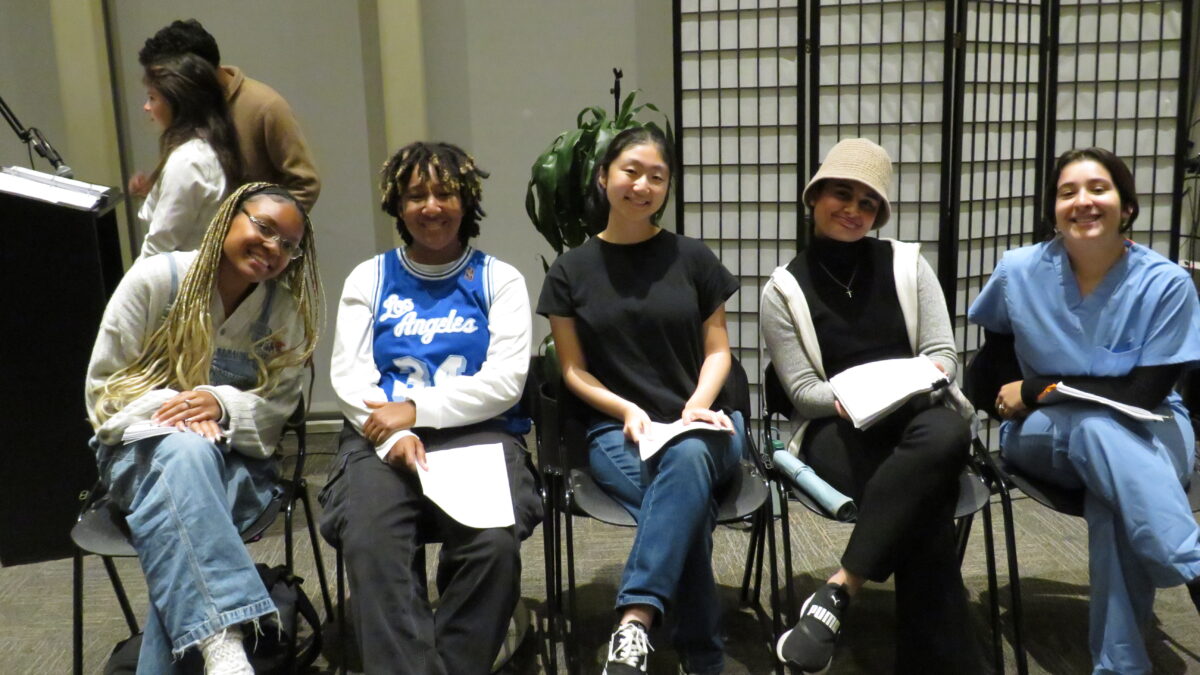 Five student-actors sit in chairs reading from manuscripts.