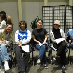 Five student-actors sit in chairs reading from manuscripts.