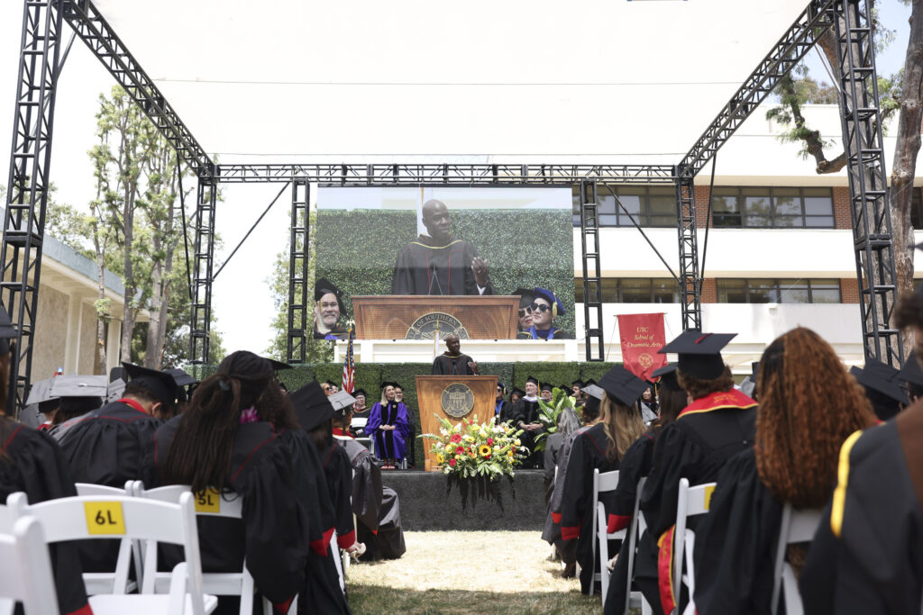 Commencement speaker McKinley Belcher III delivers his commencement address in front of a large screen.