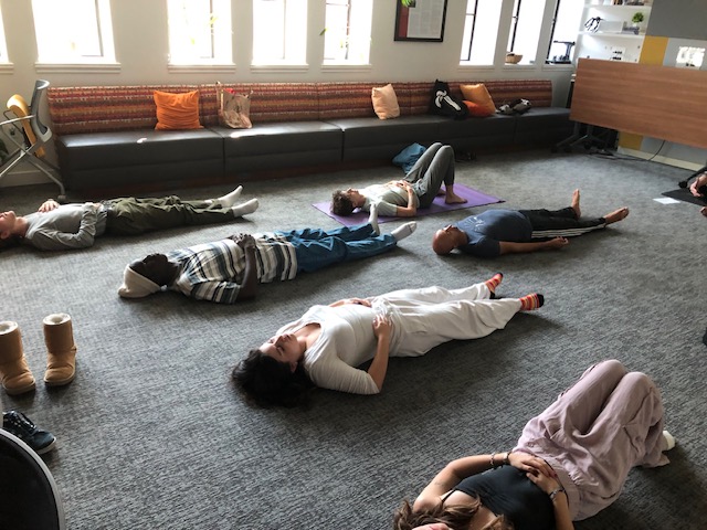 Students and community members lying on their backs on yoga mats, meditating.