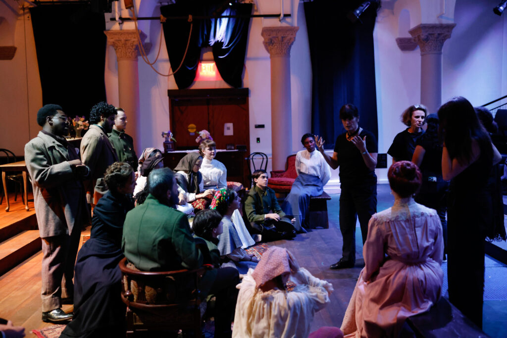 Woman in black speaking to a cast gathered.