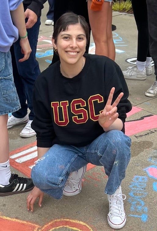Aerin Rose Glaser smiles while crouching outdoors, wearing a USC sweatshirt.